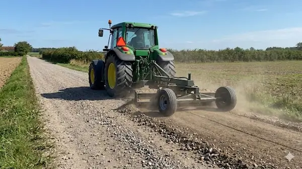 Grøn traktor på grusvej med slæbeudstyr